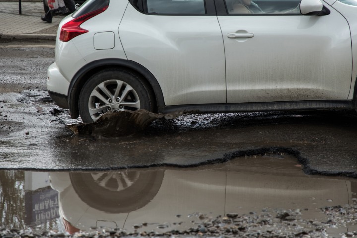 White car passing through a pothole.