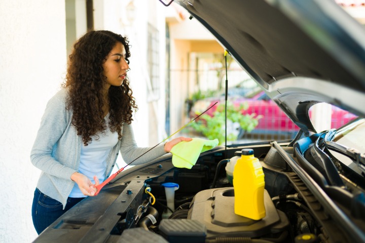 Young woman changing the oil of her car .