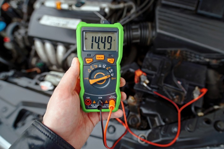 Hand with multimeter testing alternator charge level on car battery 